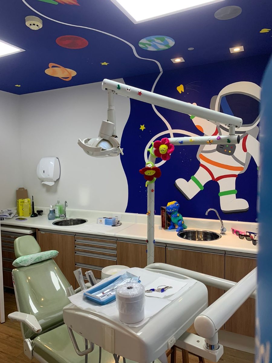 Cadeira odontológica na sala infantil, com parede azul-marinho pintada com planetas